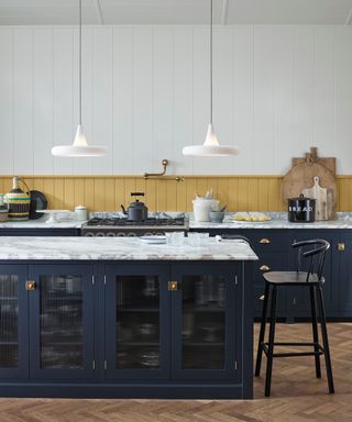 low hanging white pendant lights over kitchen island with marble top and navy and glass front doors