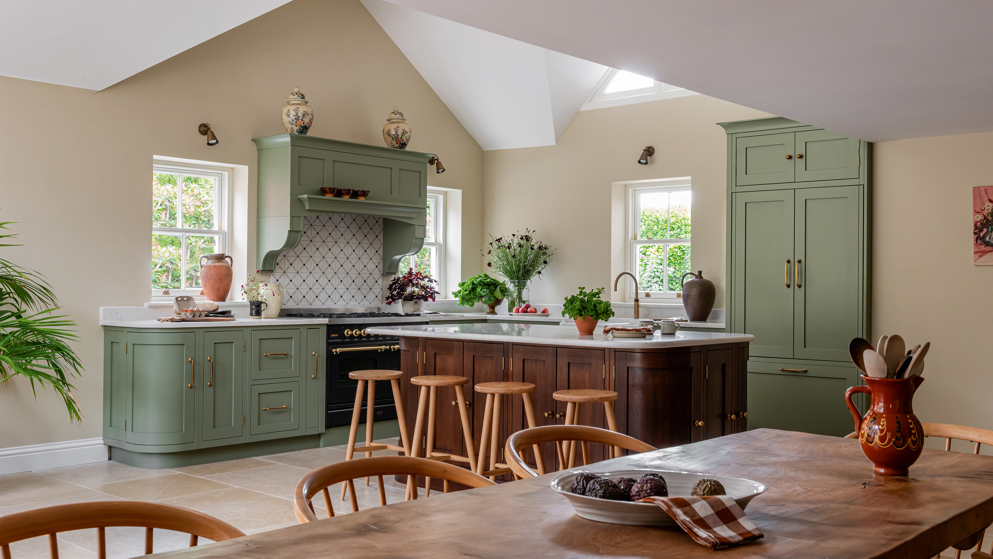 chairs and table in kitchen with cream wall green cabinetry and wooden curved kitchen island with stools