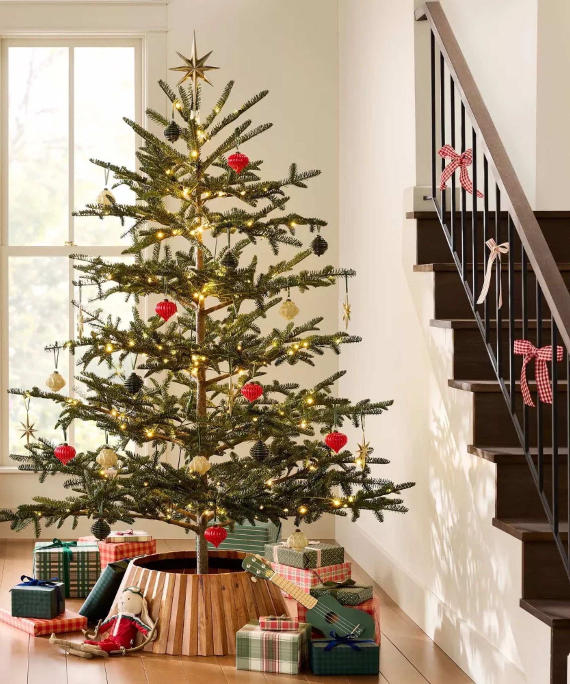 Living room with staircase, large christmas tree, red and white decorations and presents under tree