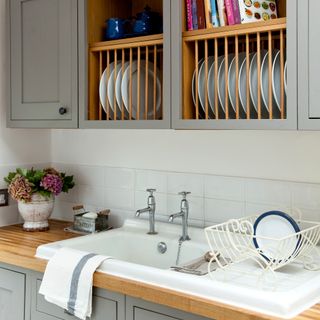 A kitchen with a sink and a plate storage shelf