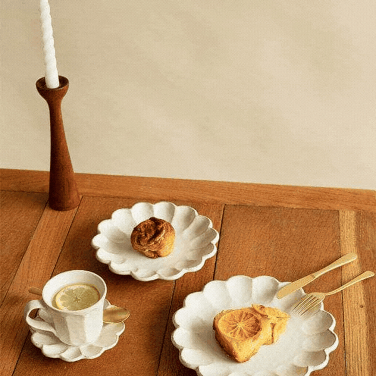 A rotating gif showcasinga floral-shaped ceramic plate against a pale gray background and styled as an afternoon tea serveware set atop a rich woody surface.