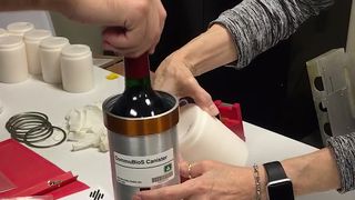 A bottle of wine is sealed inside a canister for shipment to the International Space Station.