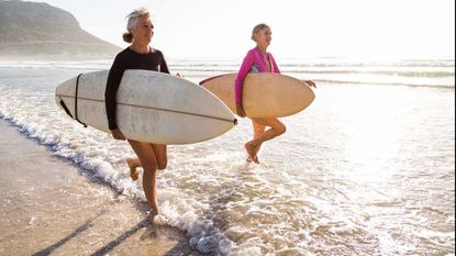 Two women walking in the ocean with their surf boards.