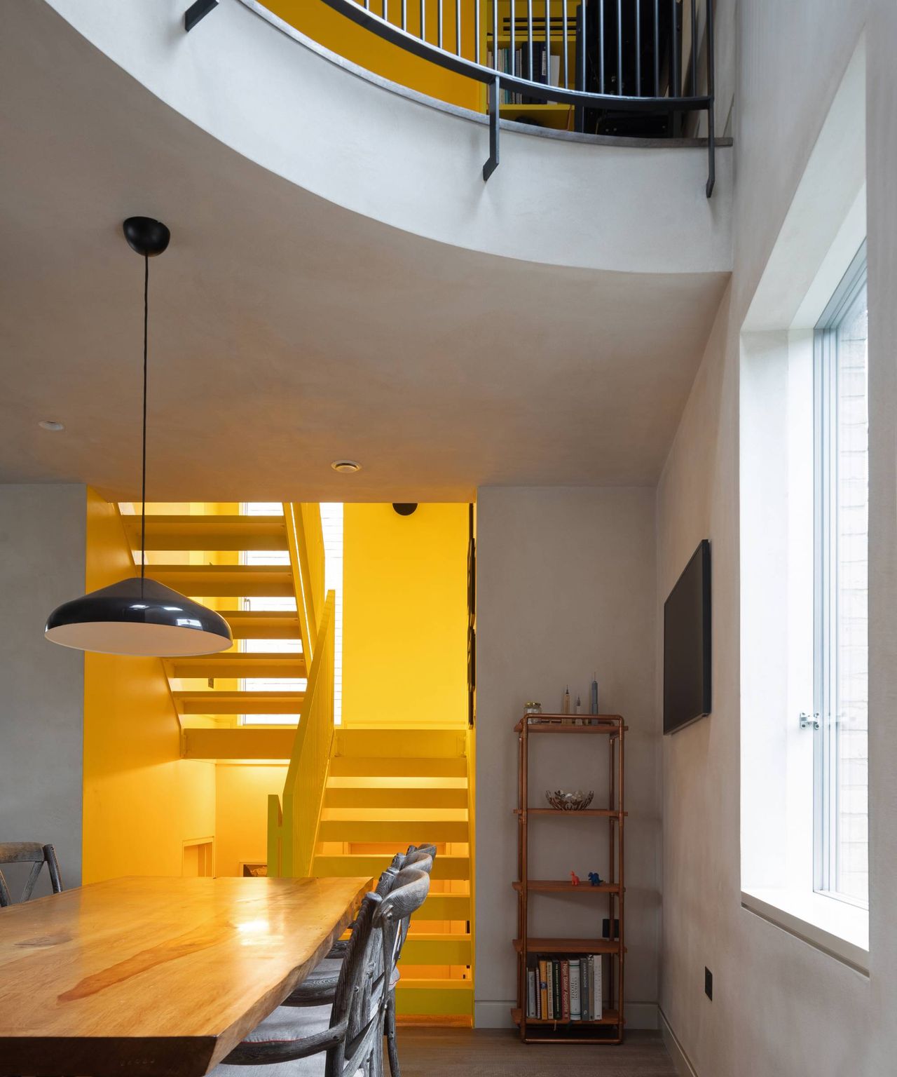inside of contemporary house with white curved mezzanine and yellow stairwell and stairs