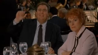 John Candy waving, wearing a suit and sitting in a restaurant in Only The Lonely