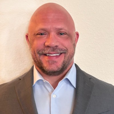 Headshot of Rick Sheets smiling and wearing gray suit jacket and light blue shirt, stood in front of cream wall.