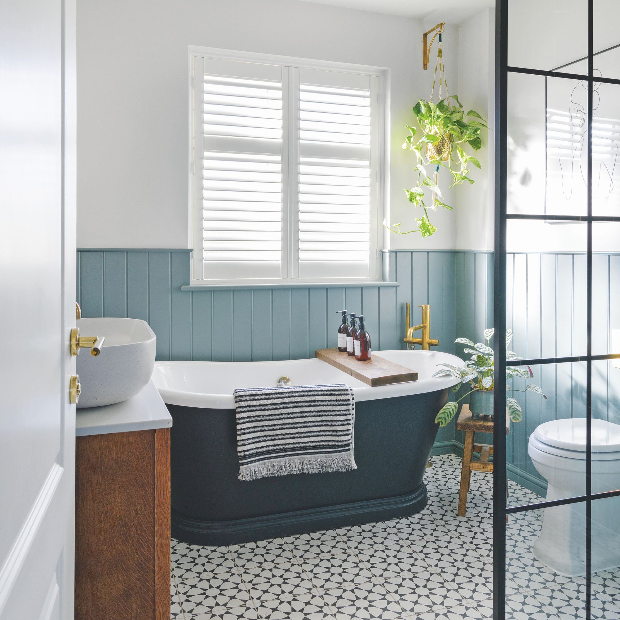 White painted bathroom with blue panelling, a dark blue freestanding bath and tiled floor