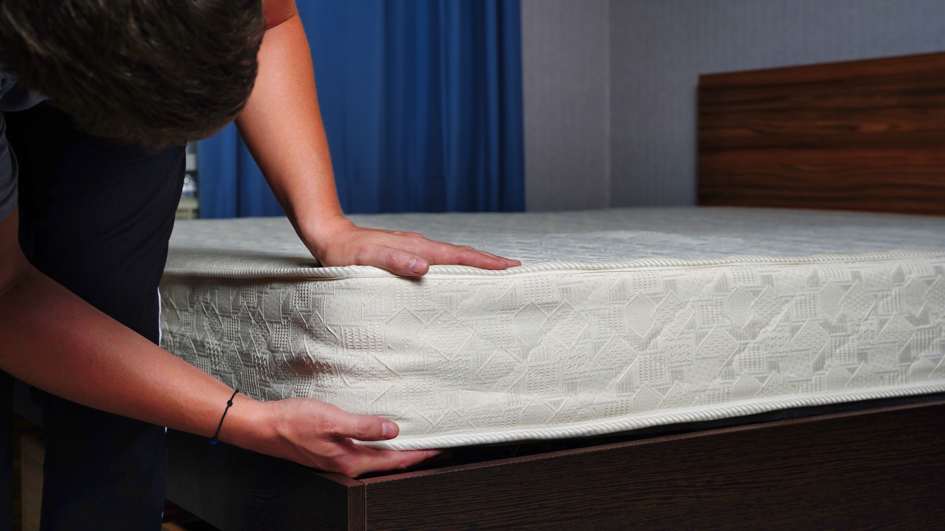 A man lifts a corner of a mattress off a black bed frame