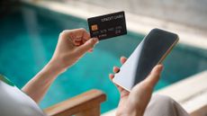 Young woman holding credit card and using smart phone sitting at hotel. 