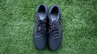 Two black football boots, both with a black sole and black laces sit side by side on green artificial grass. Kipsta Viralto IV Pro