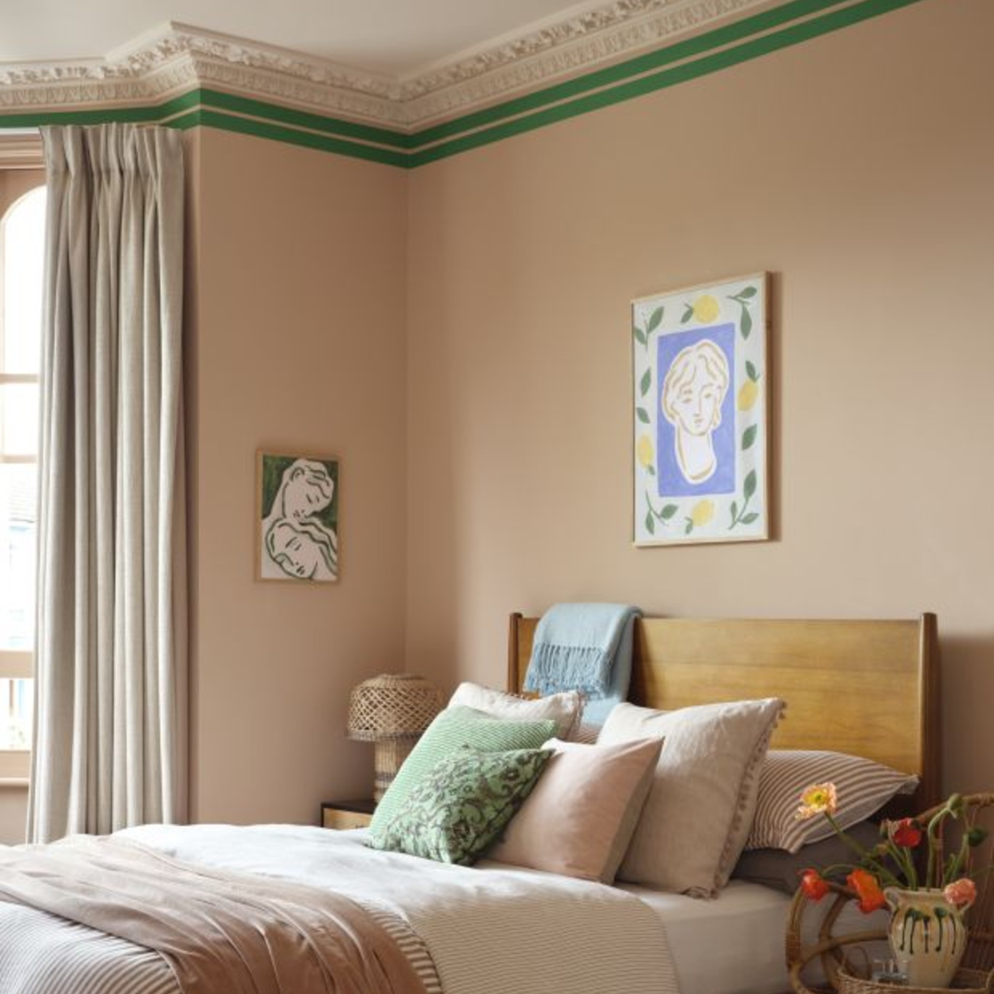 A bedroom painted in a soft pink shade with ceiling stucco detailing highlighted by two painted green stripes