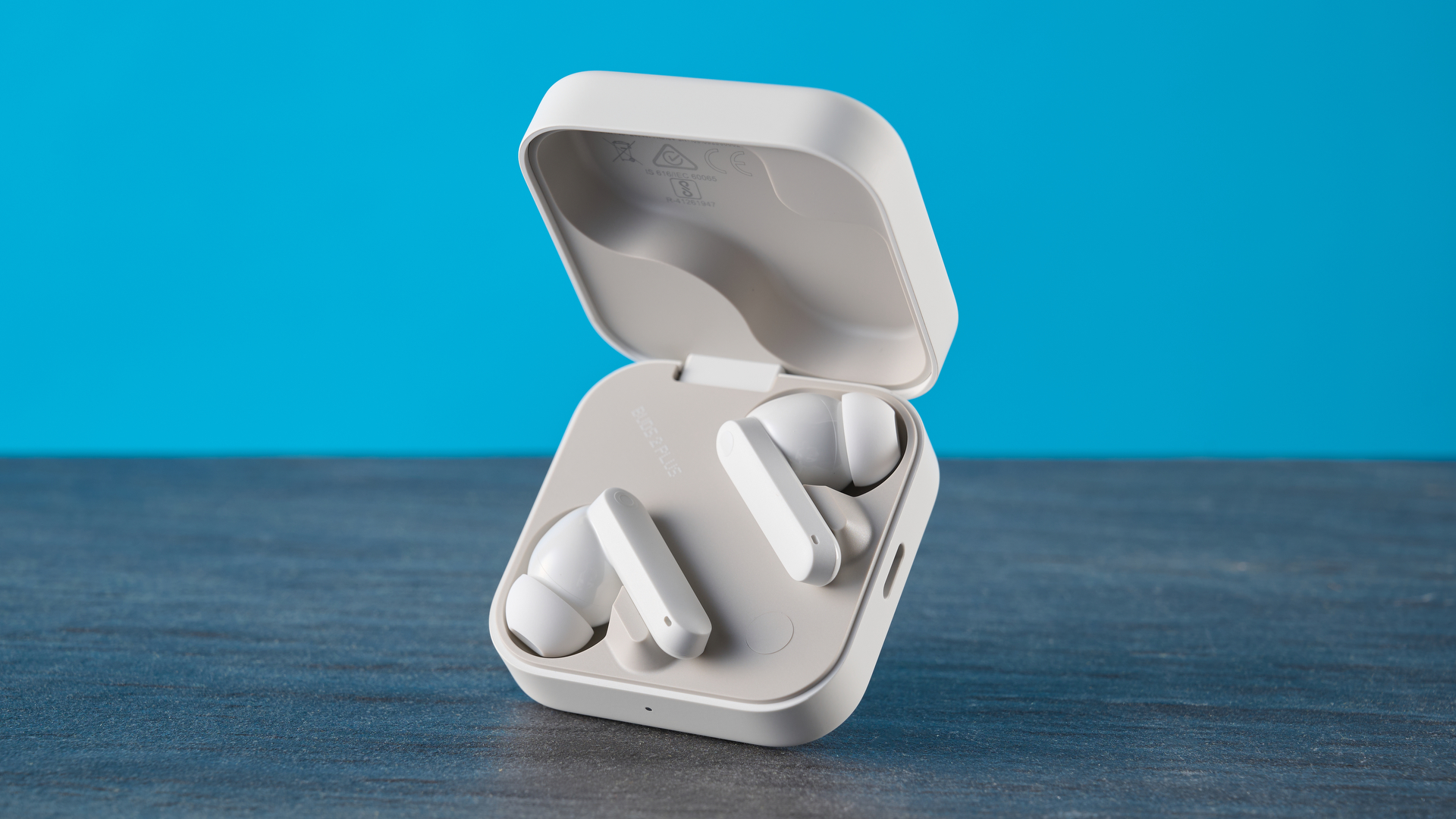 CMF Buds 2 Plus in light gray photographed in front of a blue background