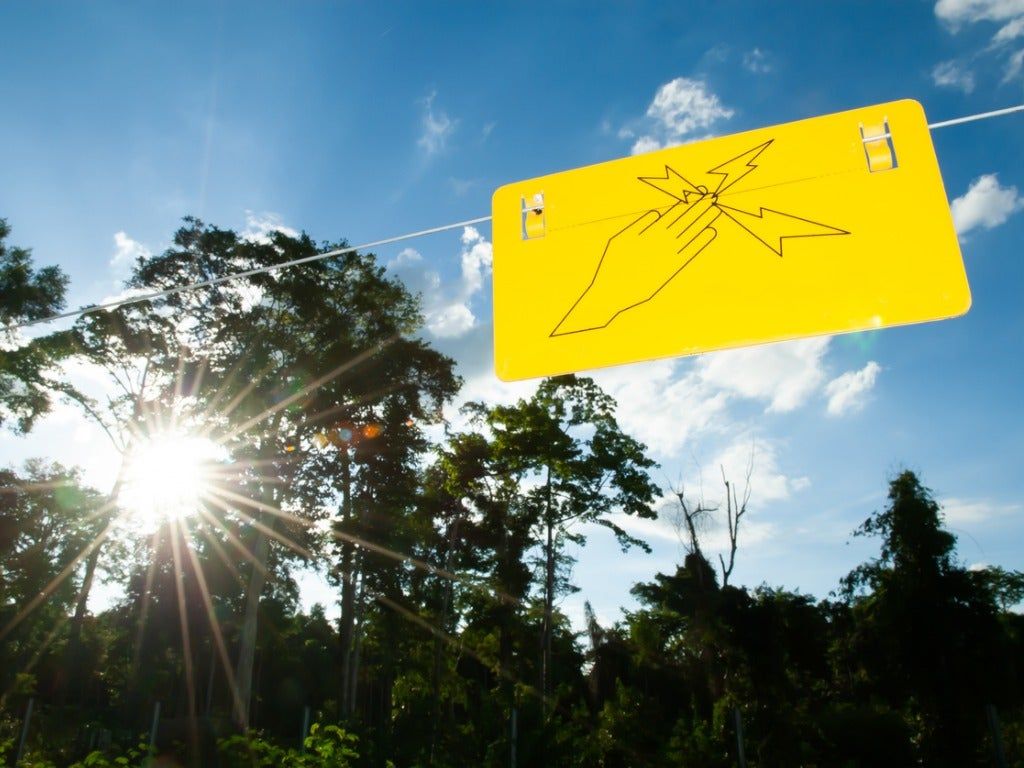 Electric Fence In Garden With Yellow Warning Sign