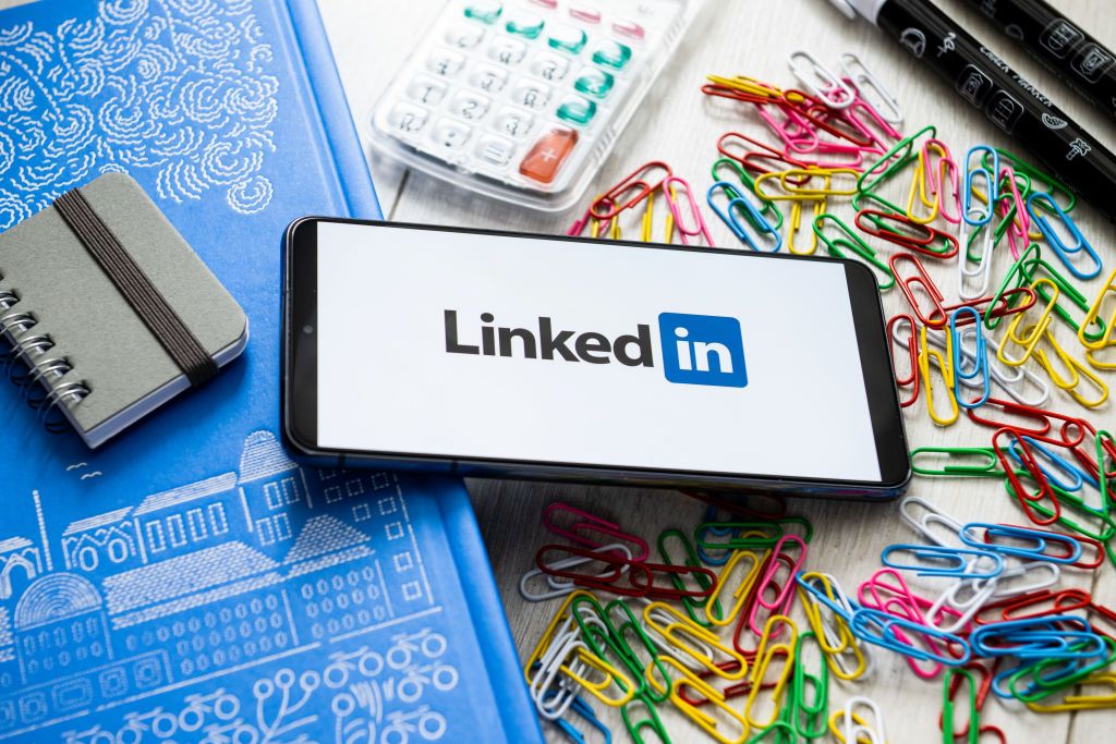 A smartphone with the LinkedIn logo displayed on screen, lying on a desk surrounded by office supplies