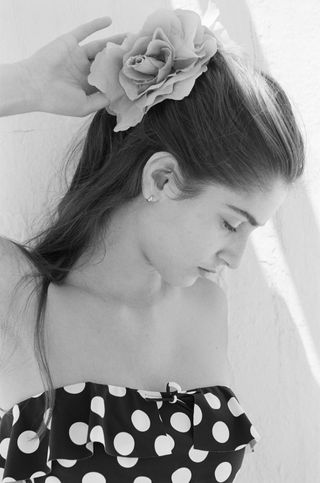 a model wears a black and white polka dot swimsuit and ruffled flower scrunchie