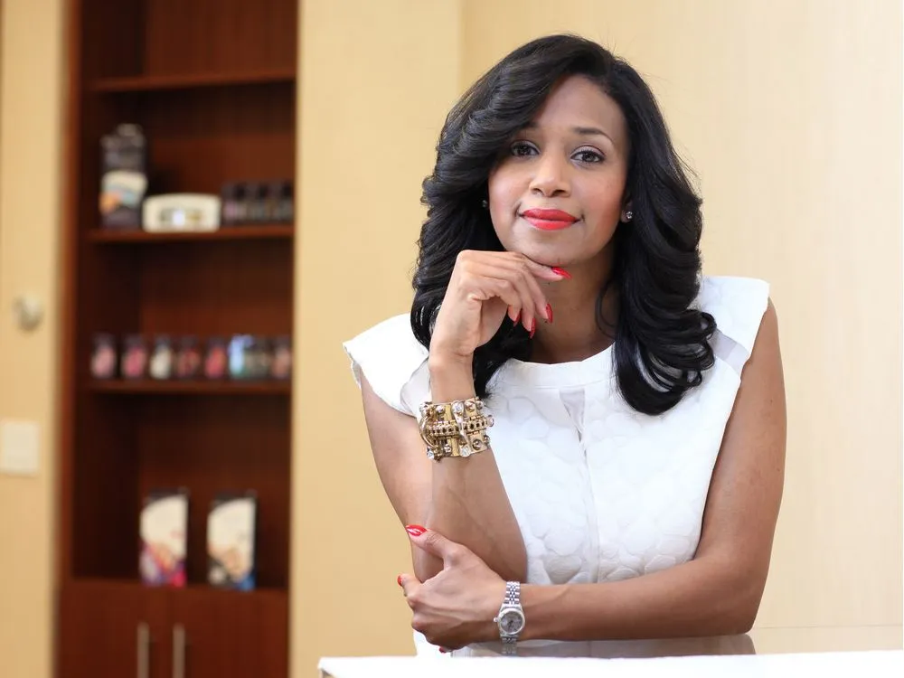 a professional headshot of a black woman with dark hair. she is wearing a white blouse, red lipstick, and red nail polish and posing with her hand on her chin