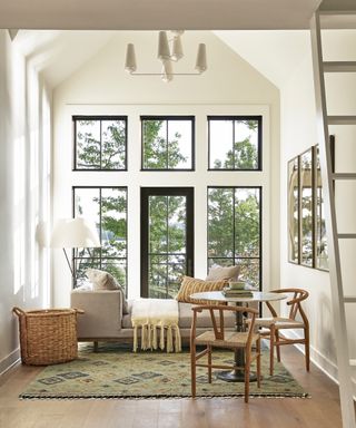 white living space with vaulted ceiling, daybed with throw and cushions, small round dining table and chairs, basket, rug, hardwood floor, floor lamp, view outside