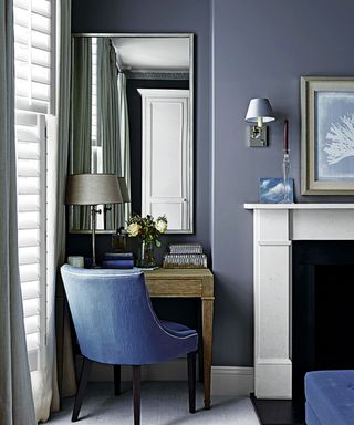 Alcove with a dressing table inset, dark grey wall with a large mirror and a blue upholstered chair.
