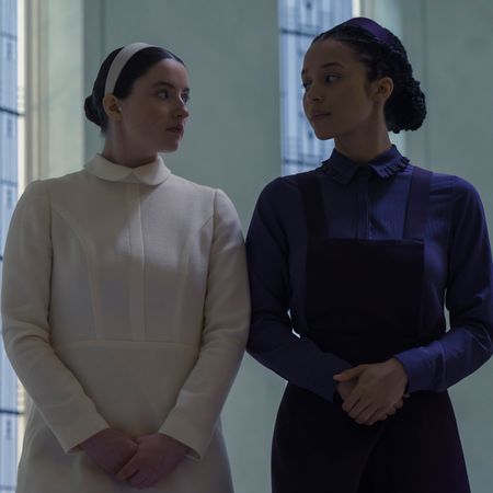 lucy halliday as daisy in white and chase infiniti as agnes in purple walking through their school hallways in the testaments