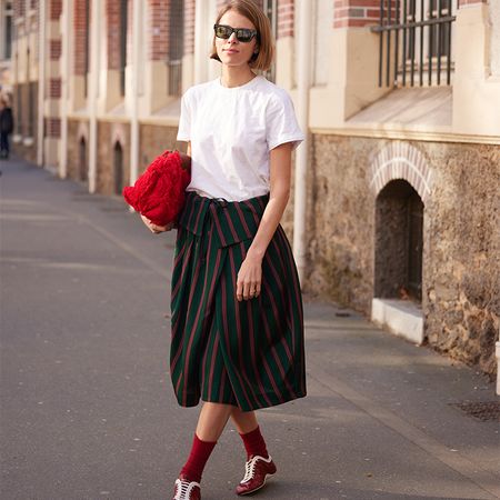 Woman wears cool skirt with fun striped pattern, red shoes, socks, and clutch with a white tee. 