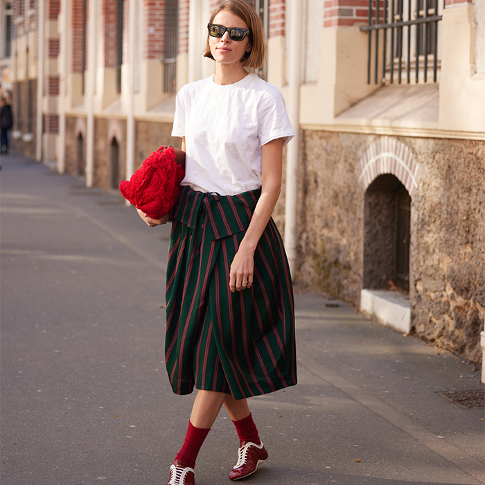 Woman wears cool skirt with fun striped pattern, red shoes, socks, and clutch with a white tee. 