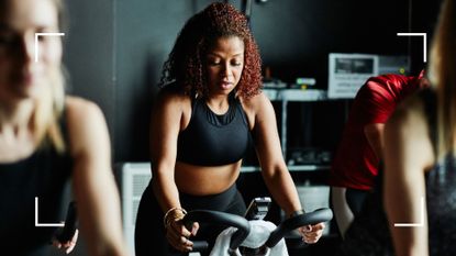 Woman looking down at exercise bike in spinning studio wearing activewear and considering cycling vs running