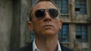 Daniel Craig walking out, wearing sunglasses, in Skyfall. 