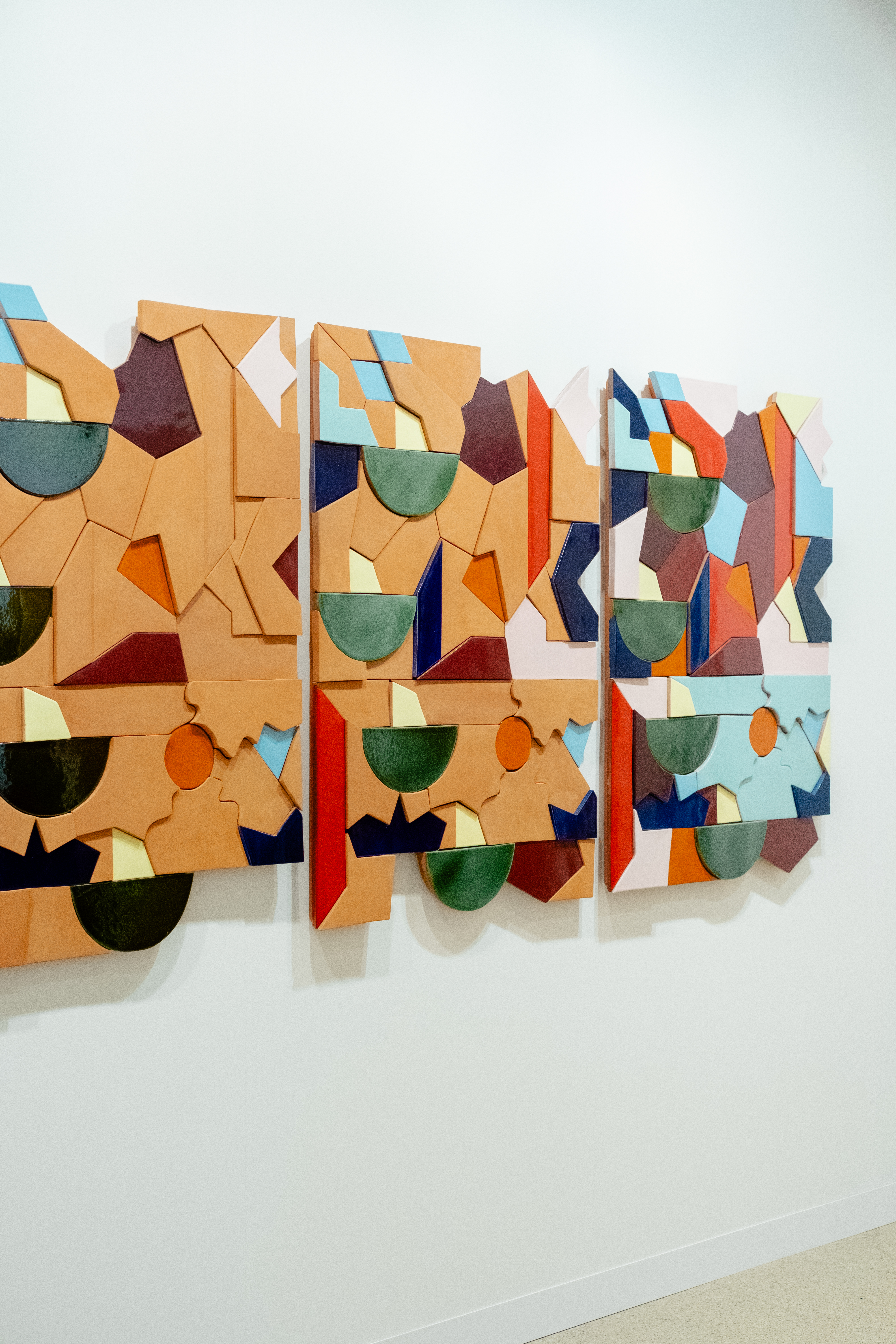 A ceramic installation made of uneven glazed and unglazed ceramic facets hangs on a white wall.