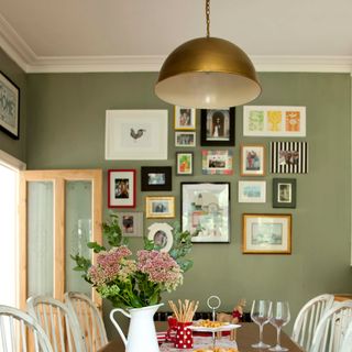 A green-painted dining room with a gold pendant light and a gallery wall