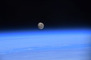 Photo of the moon rising over a blue Earth by astronaut Jessica Watkins in space.
