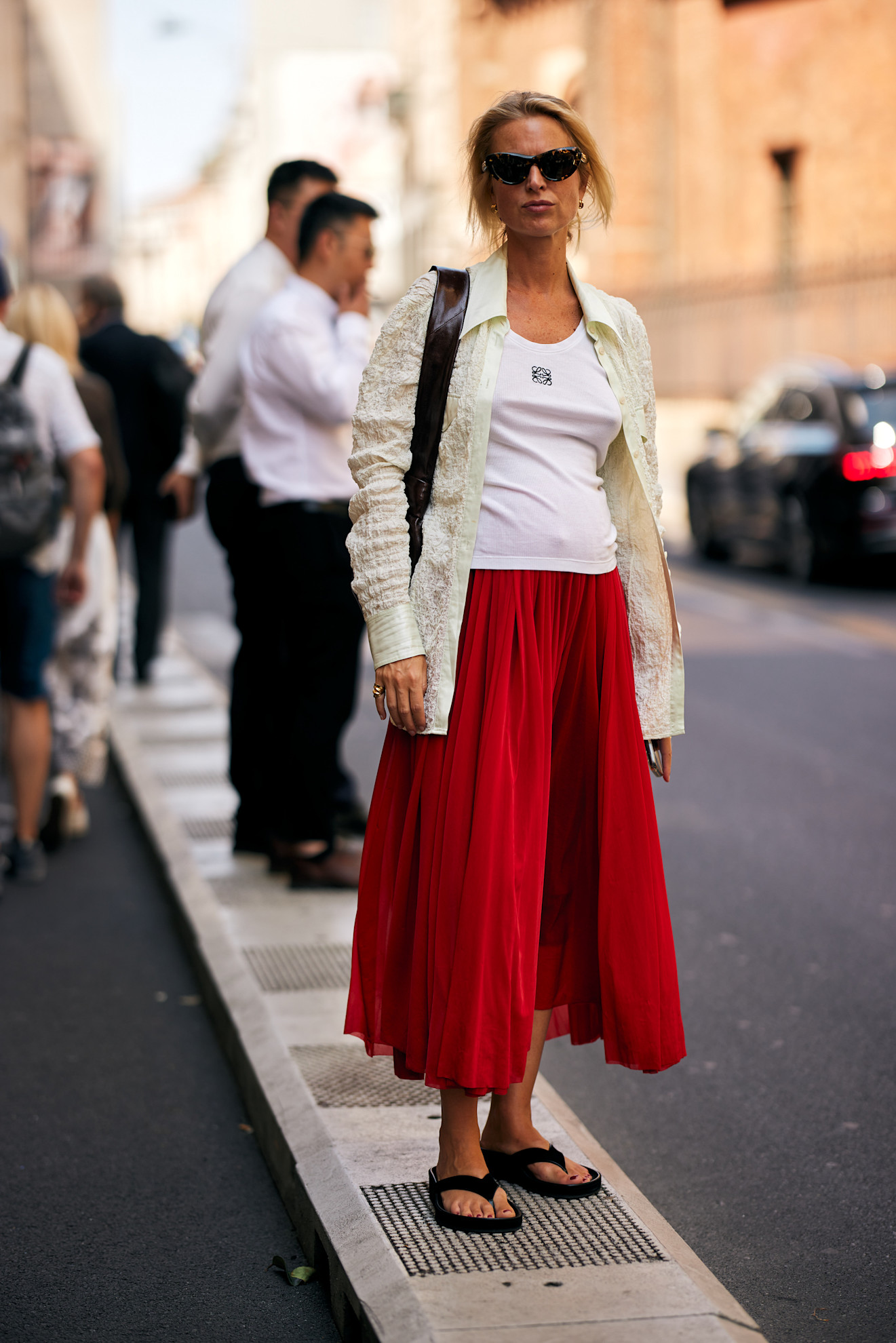 fashion week attendee wearing sunglasses, button down shirt, white tank top, red skirt, and black flip flops