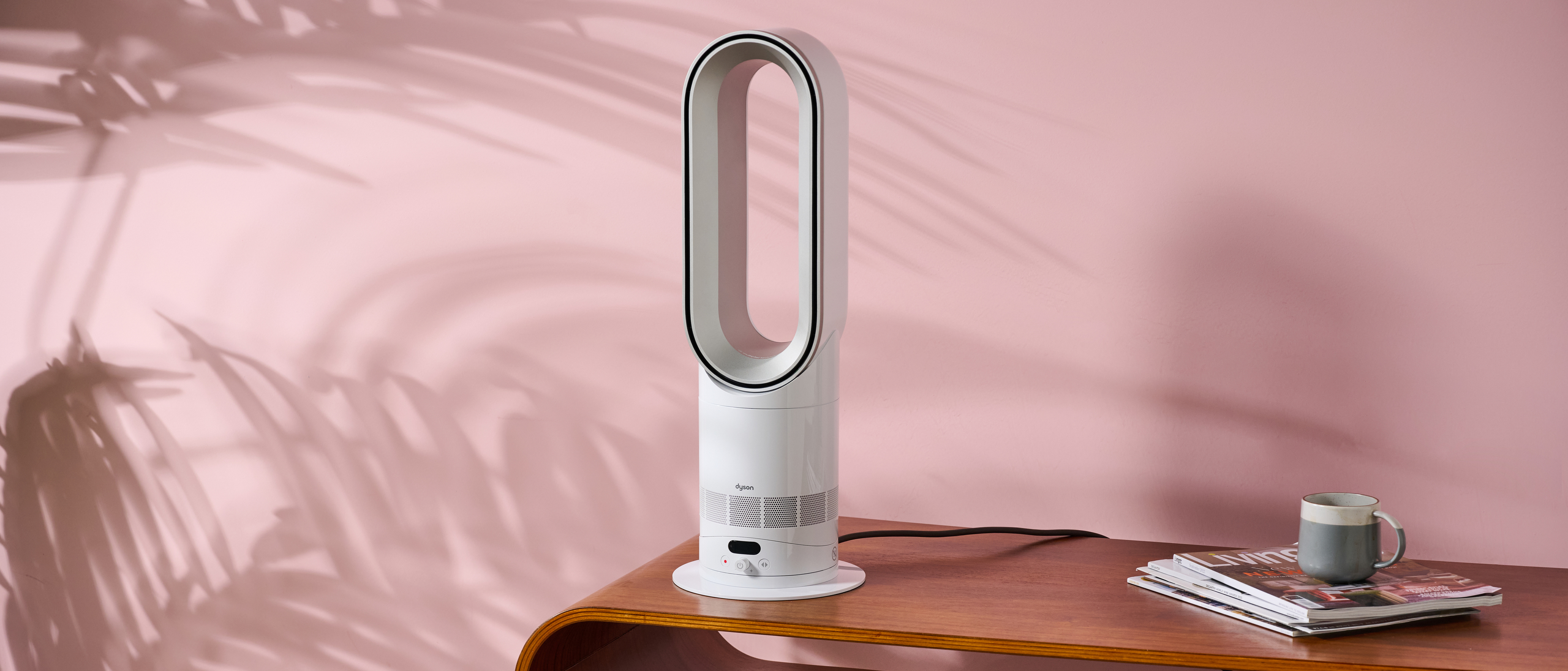 The Dyson Hot and Cool HF1 is sitting on a coffee table in a pink living room. 