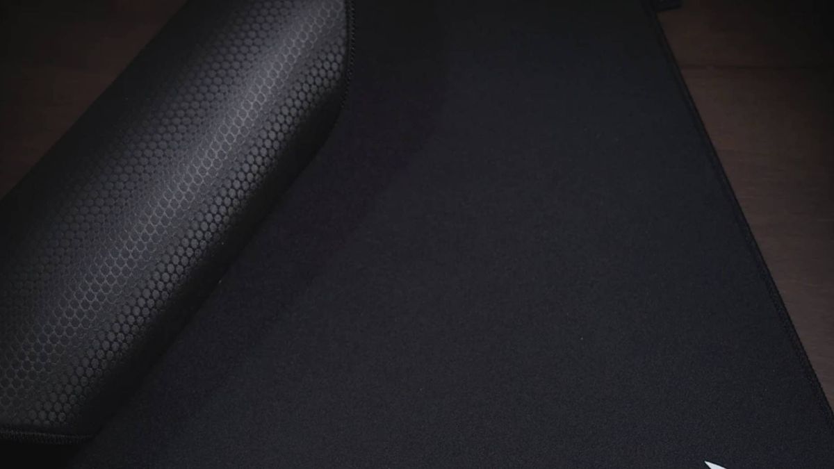 A Corsair MM Pro mouse pad on a desk being rolled up.