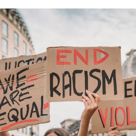 People are marching on strike against racism in the city. They are holding cardboard signs.