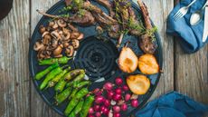a table grill with food on on a wooden surface surrounded by cutlery