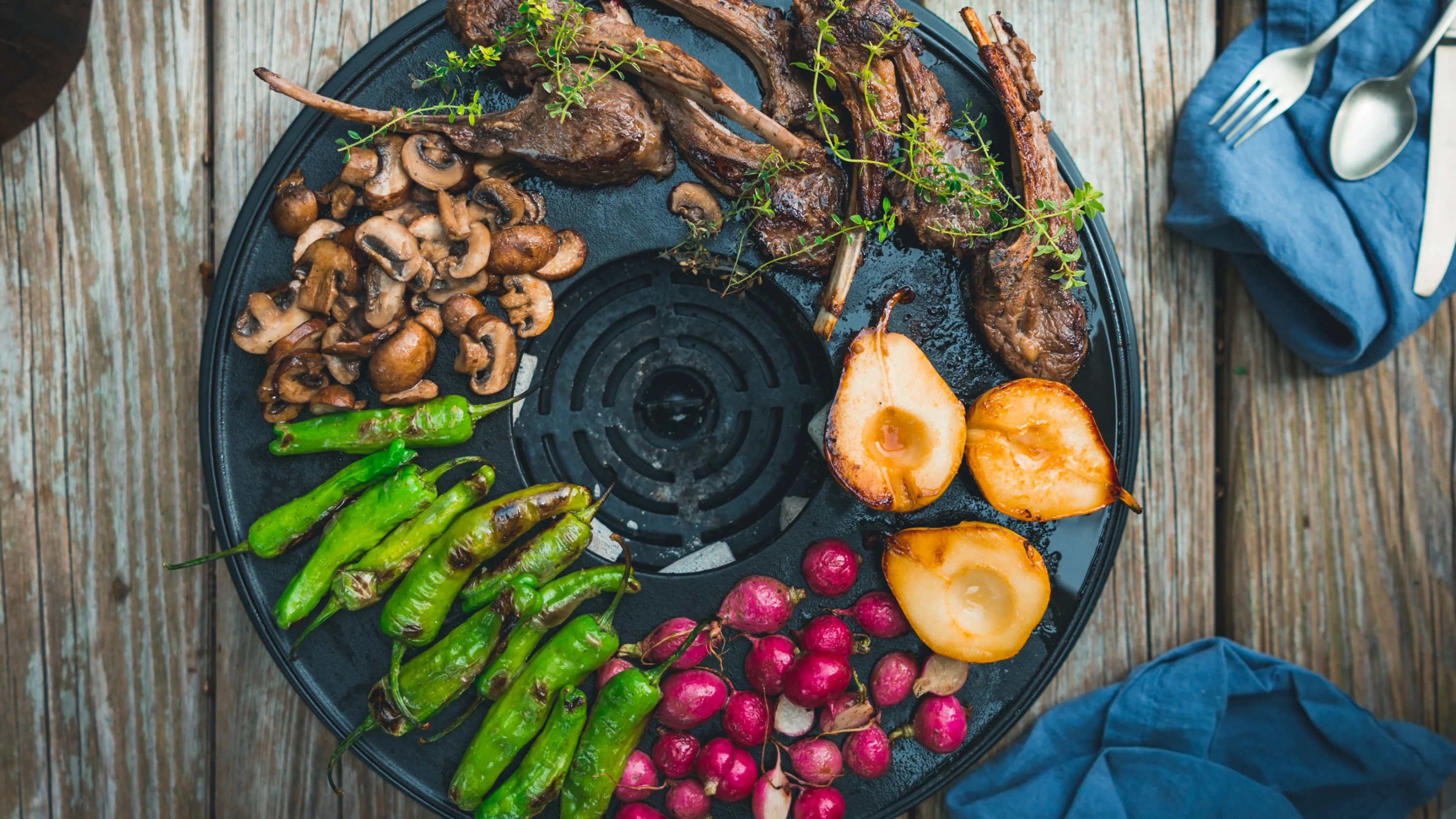a table grill with food on on a wooden surface surrounded by cutlery
