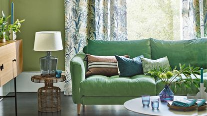 Green living room with green sofa, wicker side table, and floral curtains