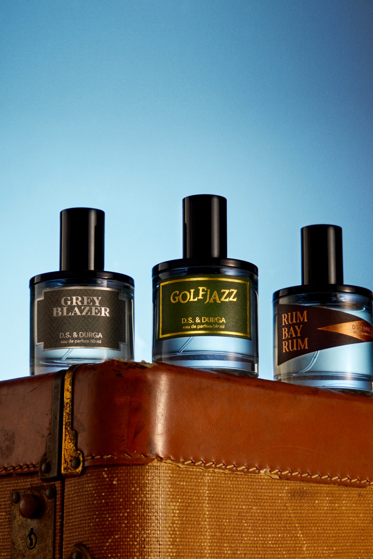 three bottles of perfume on a leather box with a blue background