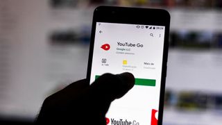 A person holding a smartphone with the YouTube Go app download page displayed