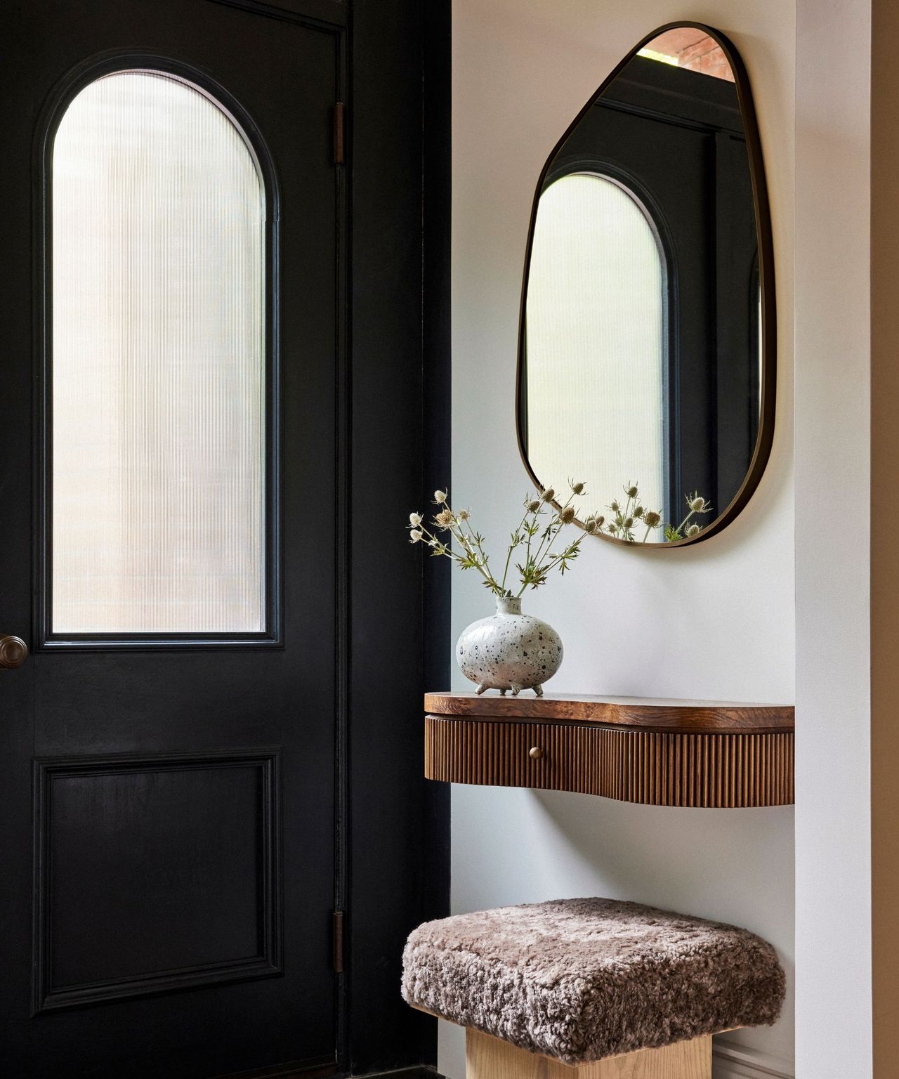 A brownstone entryway with a sculptural mirror, mounted table and stool