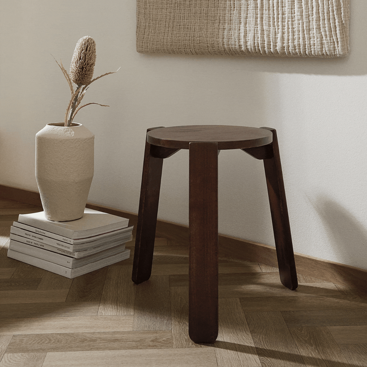 Rotating gif depicting a minimalist wooden stool, shown either sitting in a neutrally decorated living room with wooden pale floors or in an aerial product shot depicting its top.