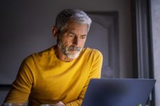 Serious mature man using laptop while sitting at home.