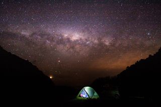 An illuminated camping tend under the milky way.