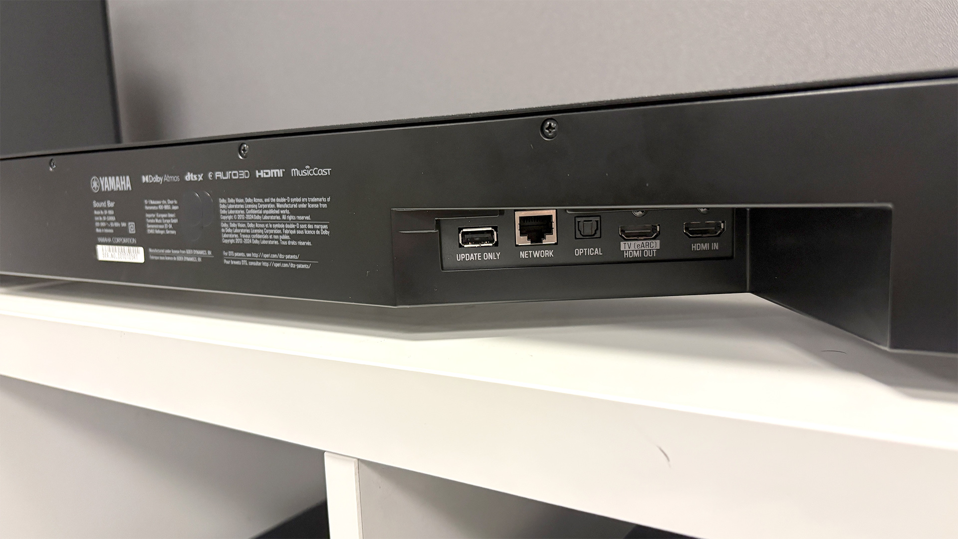 Yamaha True X Surround 90A soundbar package on white wooden shelf unit showing rear of speaker and connections