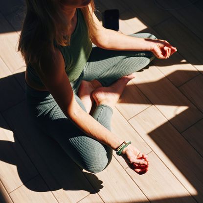 A woman meditating on the floor of a sunlit studio