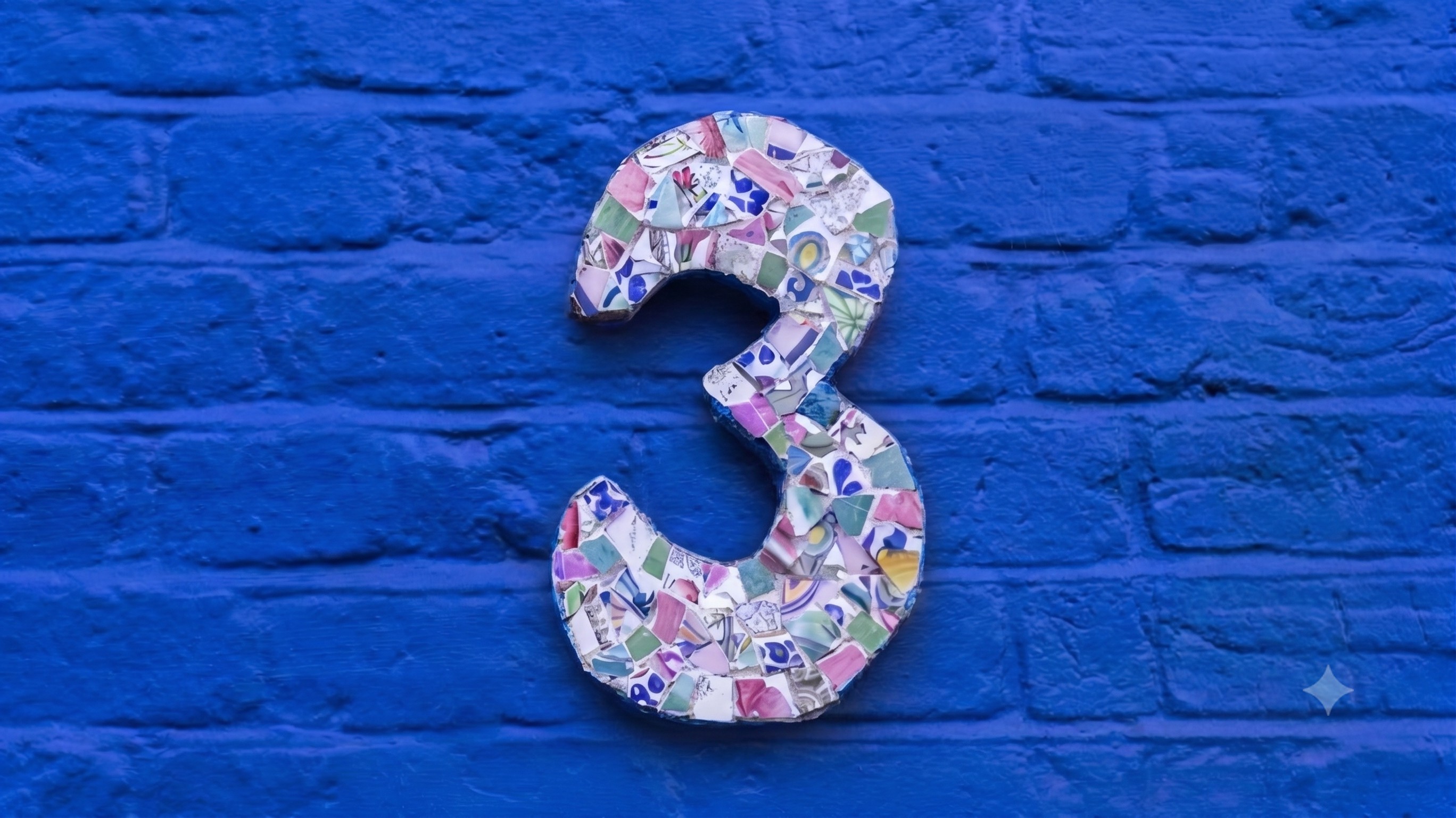 The number 3, made up of a collage of colorful broken pottery, is mounted on a brick wall painted bright blue.