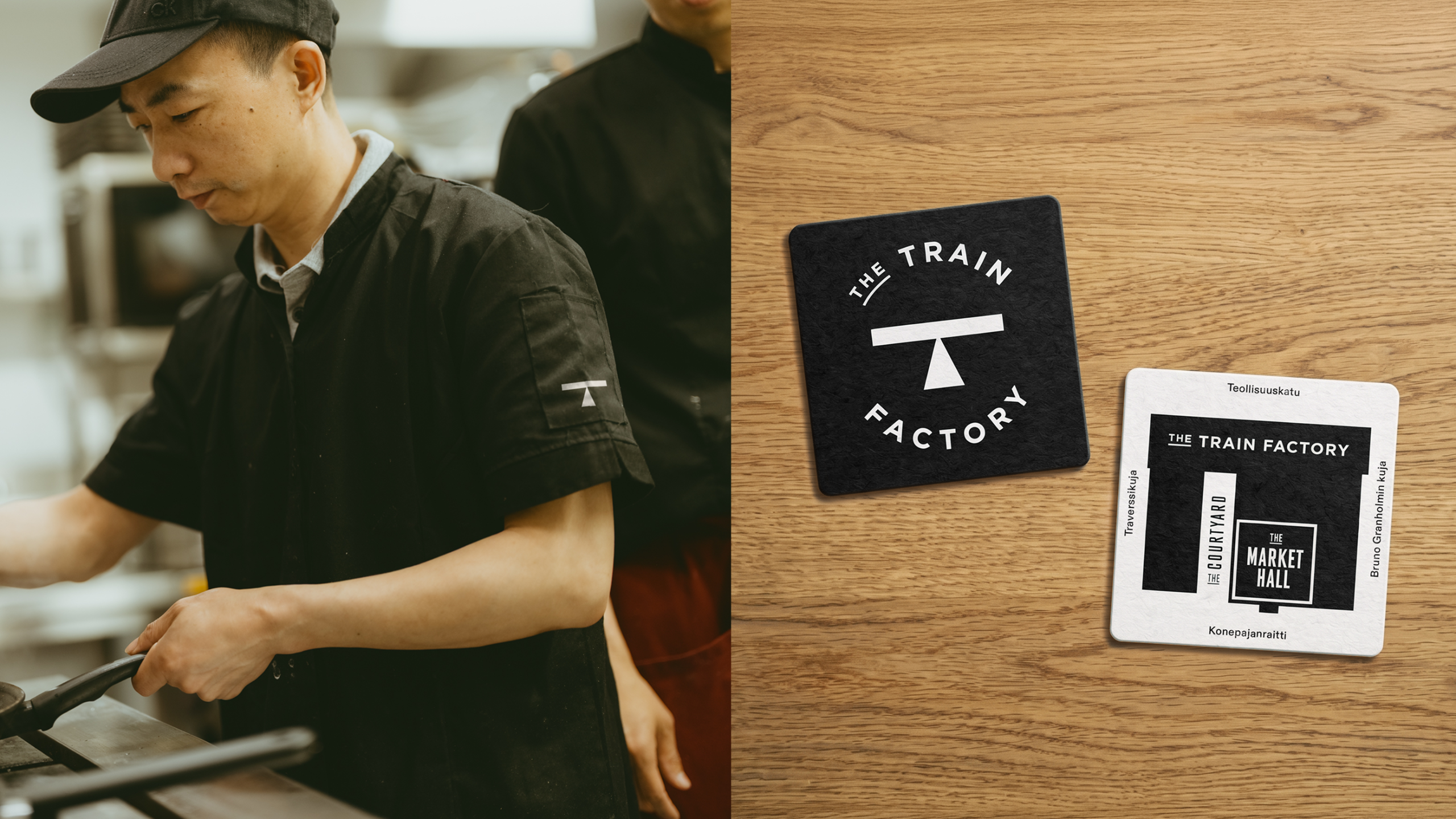A chef working in a kitchen, his sleeve embroidered with the small white "T" logo, beside a wooden surface displaying a black branded coaster and a site map coaster for The Train Factory