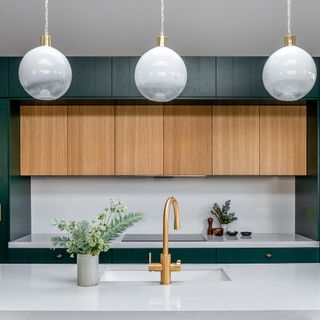 Three opaque pendant lights hanging over a white kitchen island counter with green and natural wood cabinetry visible in the background