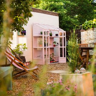 garden with half pink greenhouse, deckchairs, plants, pots, gravel