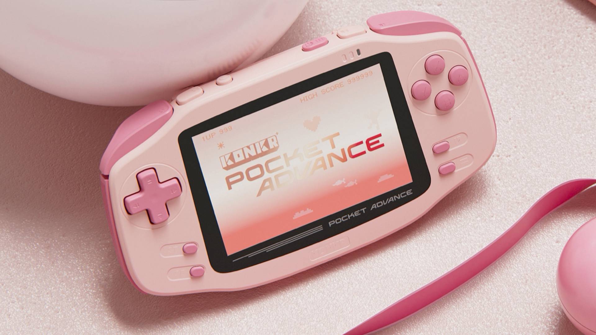 KONKR Pocket Advance handheld in pink next to link balls and ribbon on pink surface.